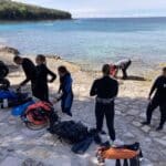 Potápěči připravující výstroj u skalnatého pobřeží průzračně modrého moře ve Vrsaru.