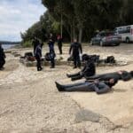 Skupina potápěčů si připravuje své vybavení poblíž břehu jezera ve Vrsaru, přičemž někteří stojí a jiní leží na kamenné cestě.